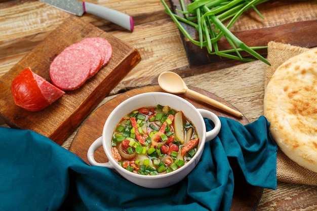 Soupe aux haricots de cuisine juive cholit sur une serviette bleue à côté d'une saucisse de pain plat et d'oignons verts