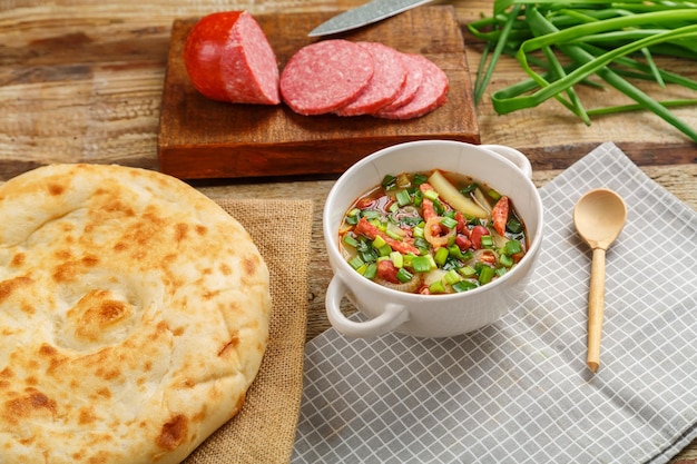 Soupe aux haricots de la cuisine juive cholit sur une serviette grise à côté de la saucisse aux oignons verts et du pain plat