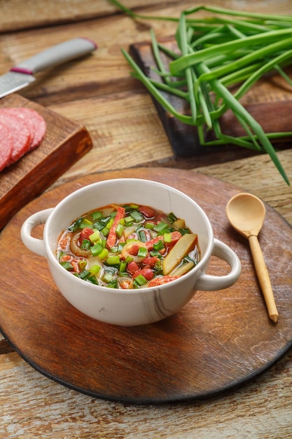 Soupe aux haricots de la cuisine juive cholit sur un support rond près des ingrédients du pain et d'une cuillère en bois