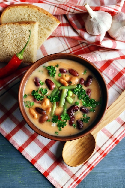 Soupe aux haricots dans un bol avec du pain frais tranché sur une serviette sur fond de table en bois