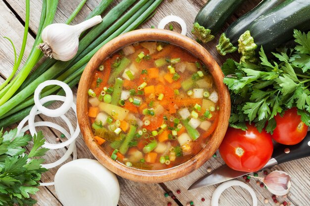 Soupe aux légumes dans un bol en bois et ingrédients sur la vue de dessus de table rustique en bois