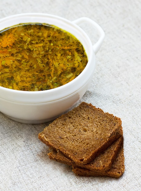 Soupe aux légumes et trois morceaux de pain sur une table