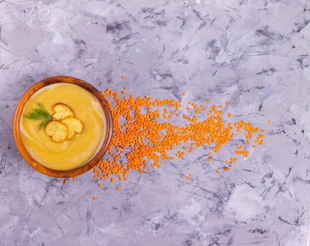 Soupe aux lentilles et à la crème de potiron à l'aneth dans une assiette en bois avec une cuillère en bois avec des lentilles orange dispersées