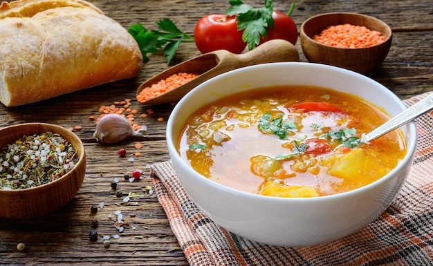 Soupe aux lentilles rouges sur la table en bois rustique avec légumes, épices et pain fait maison.