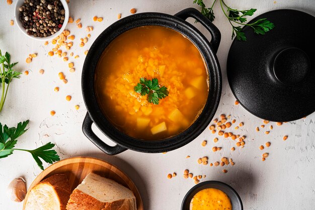 Soupe aux pois sur fond clair. Soupe dans une casserole noire. Un bol de soupe. Persil, mélange de poivre, sauce, pain. photo de haute qualité