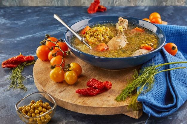 Soupe aux pois avec poulet, carottes, tomates et herbes dans une assiette creuse sur planche de bois avec serviette.