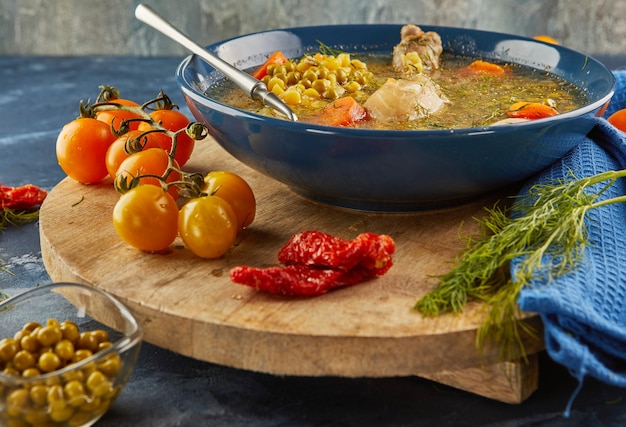 Soupe aux pois avec poulet, carottes, tomates et herbes dans une assiette creuse sur planche de bois avec serviette.