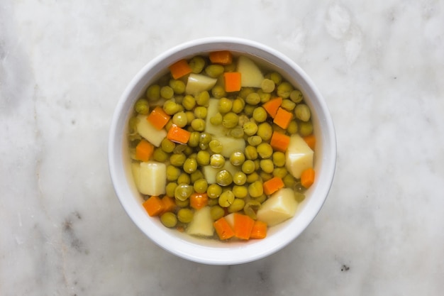 Soupe aux pois verts et légumes dans un bol blanc sur fond de marbre