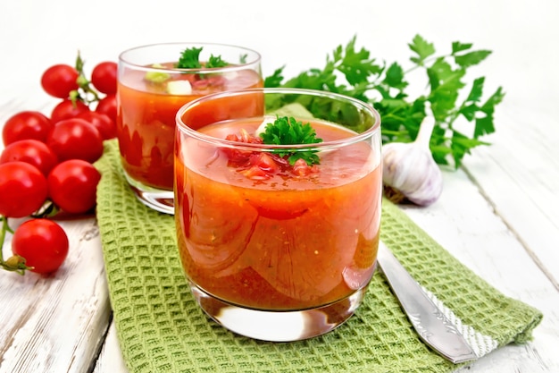 Soupe aux tomates gaspacho dans deux verres avec du persil et des légumes sur la serviette verte sur un fond de planches de bois