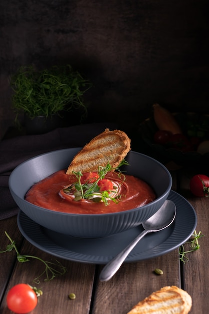 Soupe aux tomates maison dans un bol bleu avec du pain grillé sur une table en bois