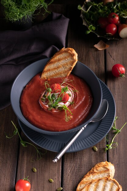Soupe aux tomates maison dans un bol bleu avec du pain grillé sur une table en bois