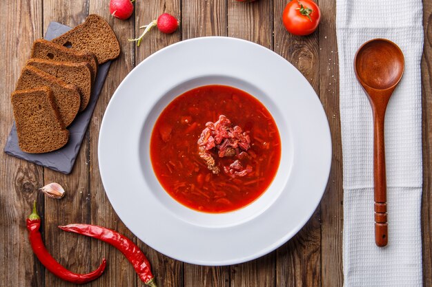 Soupe de betteraves dans une assiette blanche avec des légumes sur une table en bois. Borch, cuisine traditionnelle russe