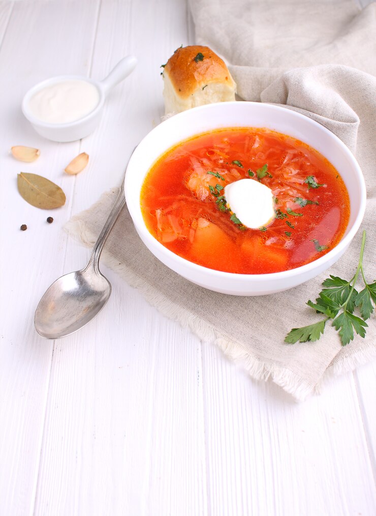 Soupe de bortsch rouge dans un bol blanc avec la crème sure et le persil, vue de dessus, sur fond blanc en bois.