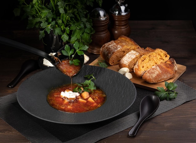 soupe de bortsch rouge sur un plat noir avec des tranches de pain et un bouquet de persil
