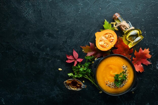 Soupe à la citrouille avec citrouille et feuilles d'automne colorées à plat Sur un fond de pierre noire Vue de dessus Espace libre pour votre texte