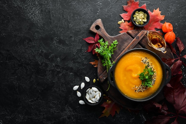 Soupe à la citrouille avec citrouille et feuilles d'automne colorées à plat Sur un fond de pierre noire Vue de dessus Espace libre pour votre texte