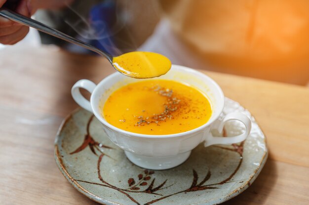 Soupe à la citrouille classique en purée à la vapeur avec garniture au poivre. Servi dans une tasse en céramique sur une table en bois.