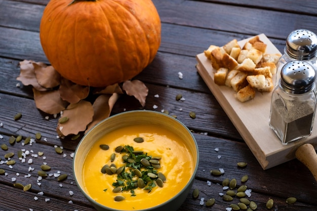 Soupe à la citrouille dans un bol sur une planche à découper en bois servie avec des graines de citrouille et des croûtons. Soupe végétalienne. Fond en bois foncé