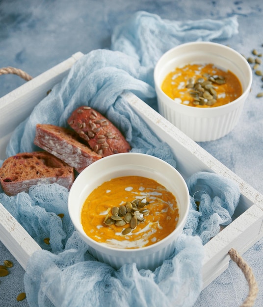 Soupe à la citrouille avec graines et crème dans un bol blanc dans une boîte en bois sur fond bleu, mise au point sélective