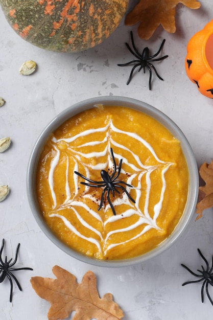 Soupe à la citrouille d'Halloween avec toile d'araignée crémeuse dans un bol gris et araignées sur la table Vue d'en haut