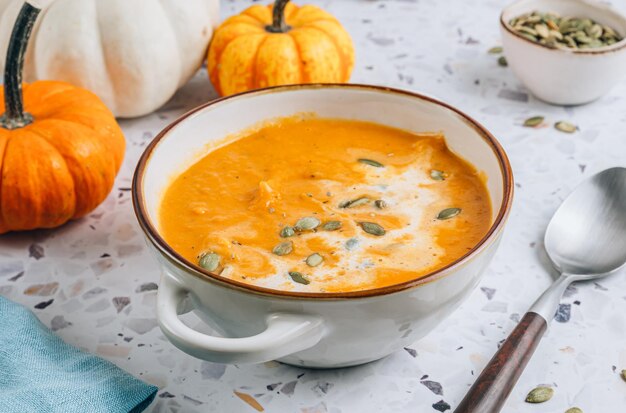 Soupe de citrouille rôtie et de carotte avec de la crème et des graines de citrouille sur fond de béton blanc Focus sélectif