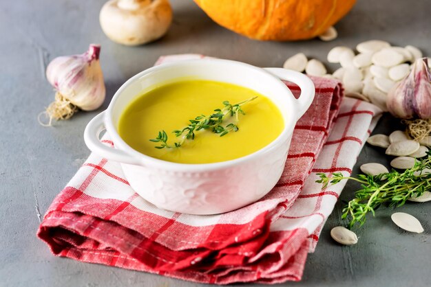 Soupe à la citrouille savoureuse avec de la crème sur fond gris Herbes de citrouille crue l'horizontale de l'ail