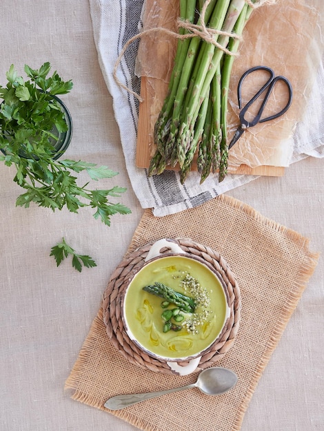 Soupe à la crème d'asperges vertes servie dans un bol à côté d'un tas d'asperges sauvages fraîches et de persil