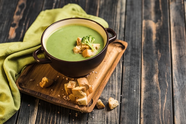 Soupe à la crème de brocoli avec croûtons dans une assiette sur une planche de service sur un fond noir en bois.