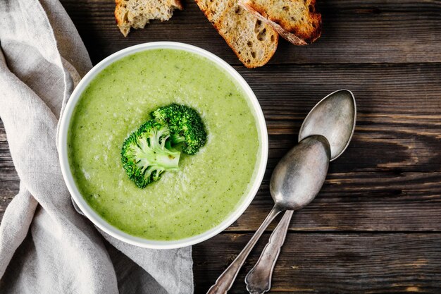 Soupe à la crème de brocoli maison dans un bol blanc avec des toasts sur fond rustique en bois Vue de dessus