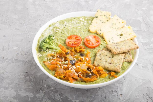 Soupe à la crème de brocoli vert avec des craquelins dans un bol blanc sur une surface en béton gris, vue latérale,