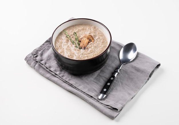 Soupe crème de champignons au thym dans un bol en céramique sur fond blanc avec cuillère