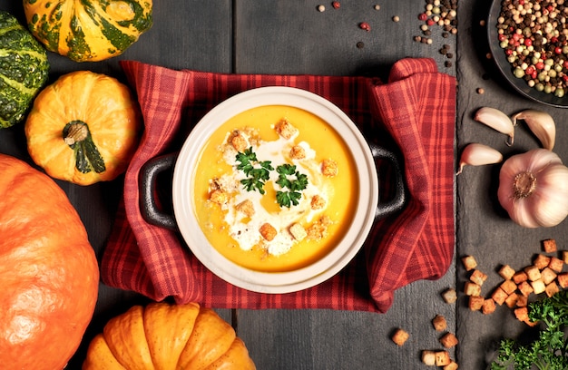 Soupe à la crème de citrouille dans un bol en céramique sombre et ingrédients sur fond noir