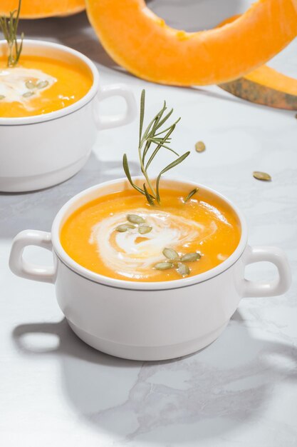 Photo soupe à la crème de citrouille avec des graines de crème aigre et du romarin dans une assiette sur un fond de citrouilles