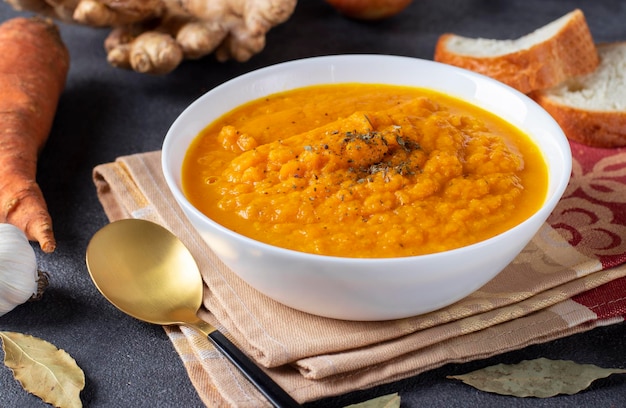 Soupe à la crème épaisse de carottes au gingembre et à l'ail dans un bol blanc sur fond sombre