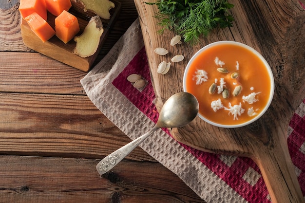 Soupe à la crème épicée à la citrouille avec du fromage et des graines sur une table en bois sur une nappe à carreaux rouge.