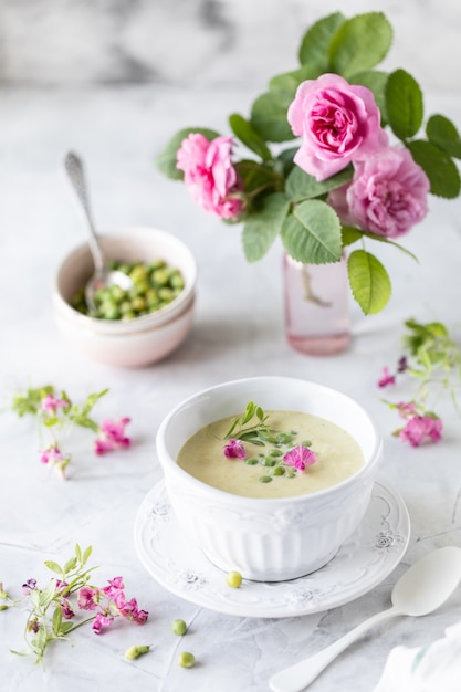 Soupe à la crème de pois verts sur une table en marbre blanc avec un bouquet de roses