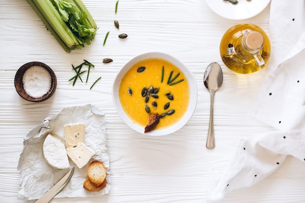 Soupe à la crème de potiron avec du fromage et des oignons sur un tableau blanc. Nature morte à plat