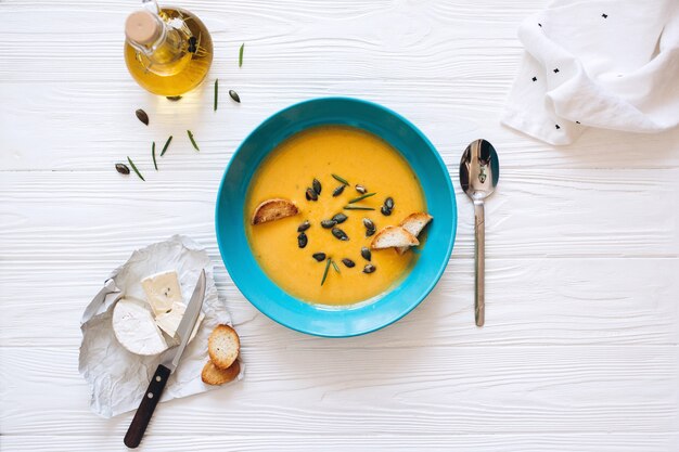 Soupe à la crème de potiron avec du fromage et des oignons sur un tableau blanc. Nature morte à plat