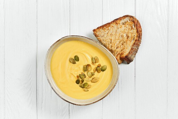 Soupe à la crème de potiron avec des graines dans une assiette sur un fond en bois blanc