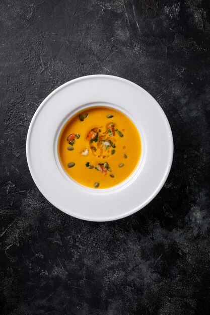 Soupe à la crème de potiron en purée dans une assiette blanche sur une table en pierre sombre