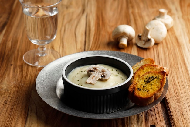 Soupe crémeuse aux champignons maison avec baguette de pain à l'ail croustillant, servir sur un bol en céramique noire ou un ramequin au-dessus d'une table rustique