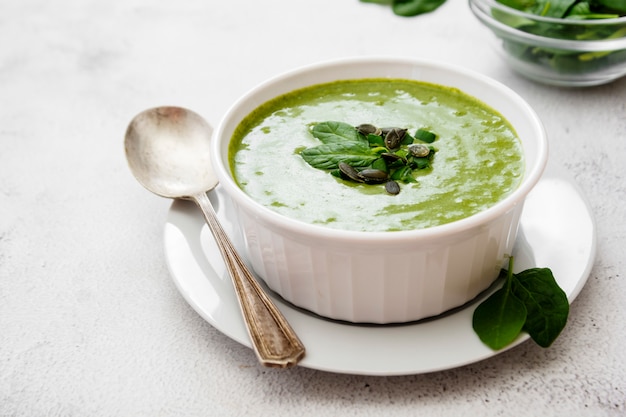 Soupe crémeuse aux épinards verts dans un bol blanc, soupe crémeuse verte saine au printemps. Détox, suivre un régime ou manger des aliments propres.