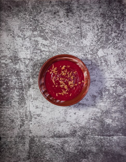 Soupe crémeuse de betteraves froides aux légumes avec chips d'oignon sur fond texturé. Soupe de bortsch à la crème alimentaire traditionnelle dans une assiette brune avec des oignons. Soupe végétalienne bortsch tomate, carotte, huile d'olive. Espace de copie