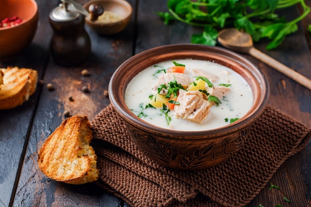 Soupe crémeuse finlandaise chaude avec du saumon et des légumes dans un vieux bol en céramique sur une vieille surface en bois. Style rustique.