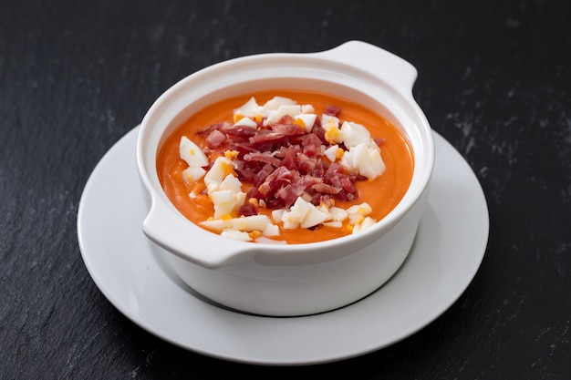 Soupe espagnole typique crème salmorejo avec jambon et oeuf dans un bol blanc sur fond en céramique