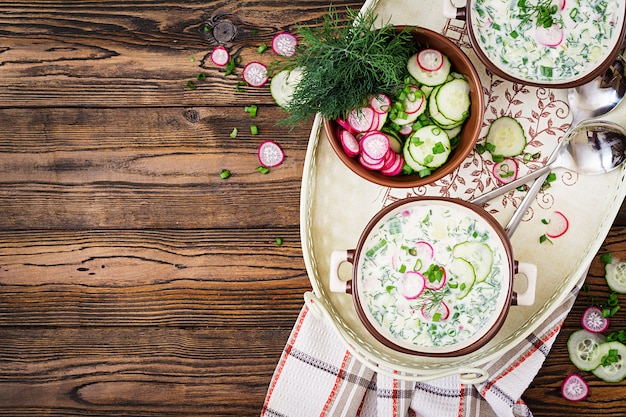 Soupe froide aux concombres frais, radis au yaourt dans un bol sur une table en bois. Cuisine russe traditionnelle - okroshka. Repas végétarien. Vue de dessus. Mise à plat