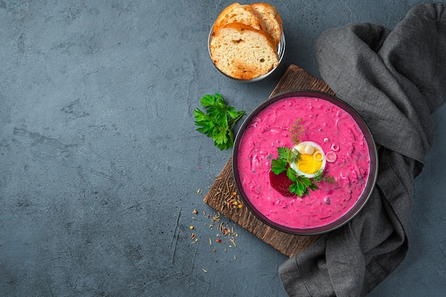 Soupe froide de betteraves rouges avec œuf, herbes, kéfir et pommes de terre sur fond gris-bleu. Vue de dessus, copiez l'espace.