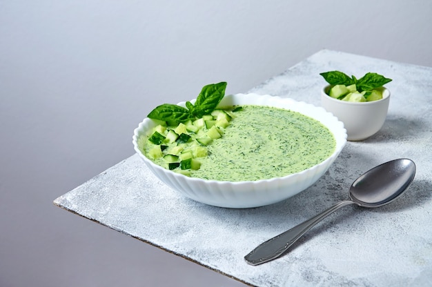 Soupe froide d'été au gaspacho de concombre au basilic dans un bol blanc sur fond clair