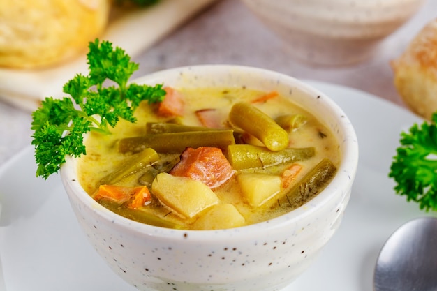 Soupe de légumes à base de haricots verts coupés, de carottes, de pommes de terre et de morceaux de jambon.