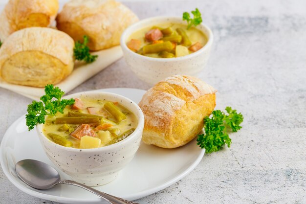 Soupe de légumes crémeuse maison fraîche sur bol blanc avec petit pain et cuillère.